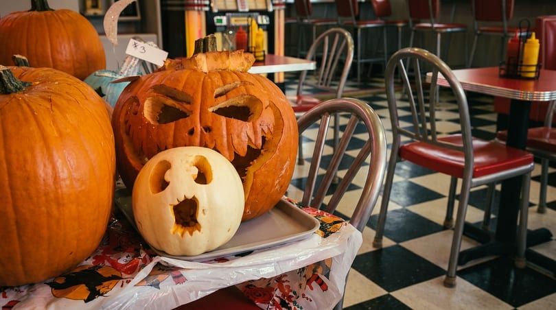 Jack-o'-lanterns and a white carved pumpkin on a chair in a diner with checkered floor.