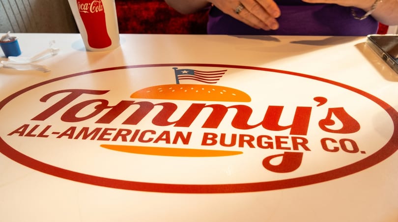 Tommy's All-American Burger Co. logo on a white table with a Coca-Cola cup and cutlery.